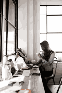 Woman working on laptop at cafe with coffee cup in hand