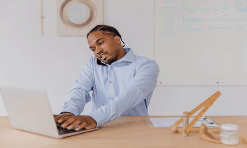 Focused professional multitasking at desk with laptop and phone in modern office setting