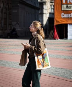 Woman holding phone and bag on city street, showing handle length and style.