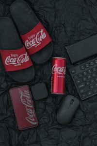 Red Coca-Cola can placed on a table among casual items and tech accessories.