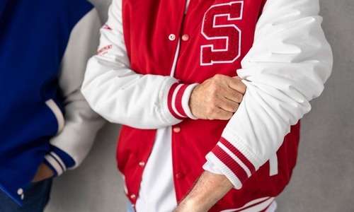 Two men standing wearing varsity jackets in casual pose on white background