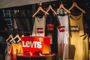Sunlit clothing store display with several Levi’s branded T-shirts hanging neatly on wooden hangers.