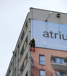 Worker installing large banner on building facade, highlighting installation and delivery services