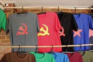 T-shirts with hammer and sickle and star logos hanging on a rack against a brick wall.