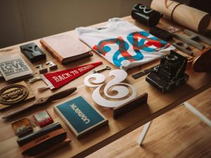 Assorted lifestyle items, including a graphic T-shirt, camera, and pennant, on a desk.