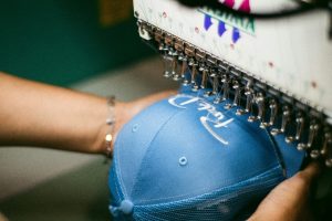 Close-up of a blue baseball cap being embroidered by an industrial sewing machine.