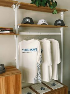 Three white T-shirts hanging on a rack, featuring 'THIRD WAVE SPECIALTY COFFEE' text