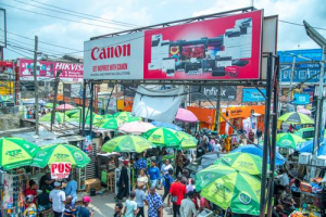 Large Canon advertising banner above a busy outdoor market offering cost-effective promotion