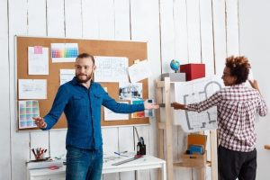 Two designers reviewing blueprints, considering factors before choosing banner dimensions.