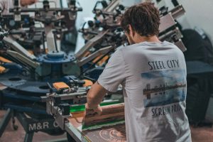 Man operating a screen printing press, demonstrating live screen printing for events