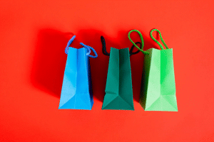 Three colorful paper gift bags in blue, dark green, and light green lined up on a bright red surface.