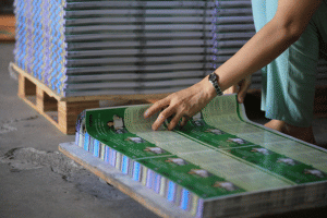 Close-up of a worker flipping through printed green paper sheets next to a pallet.