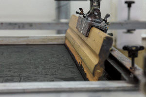 Wooden squeegee set up on a screen printing frame in a workshop.