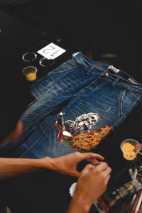 Person painting a detailed skeleton and fire artwork onto a pair of blue denim jeans.