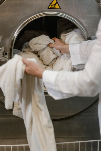 Hands pulling white towels out of a large metal washing machine drum.