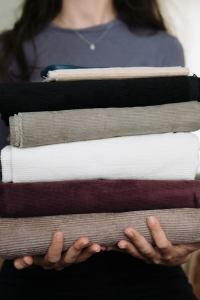 Person holding a stack of neatly folded corduroy fabric bolts in various colors.