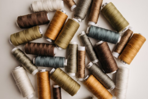 Assorted thread spools scattered on a light surface in earthy tones of green, brown, and gold.